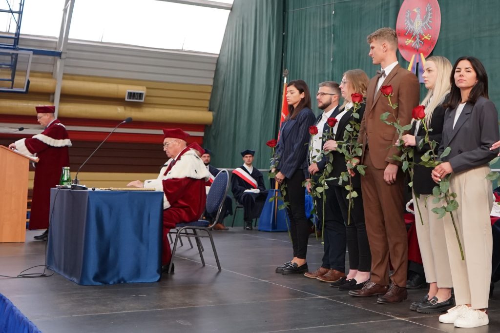 Studenci stoją w rzędzie na scenie z różami w ręku