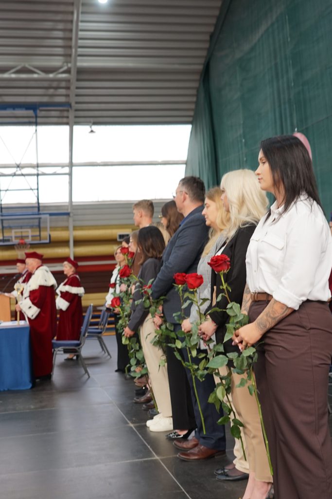 Studenci stoją w rzędzie na scenie z różami w ręku