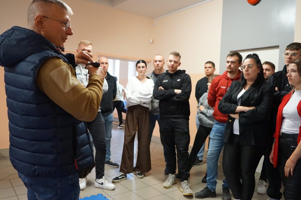 grupa studentów stoi i słucha prowadzącego