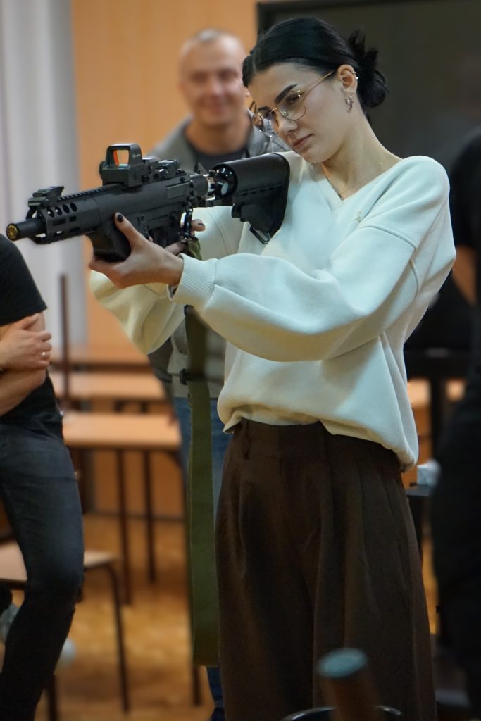 Dziewczyna w białym swetrze celuje z karabinu